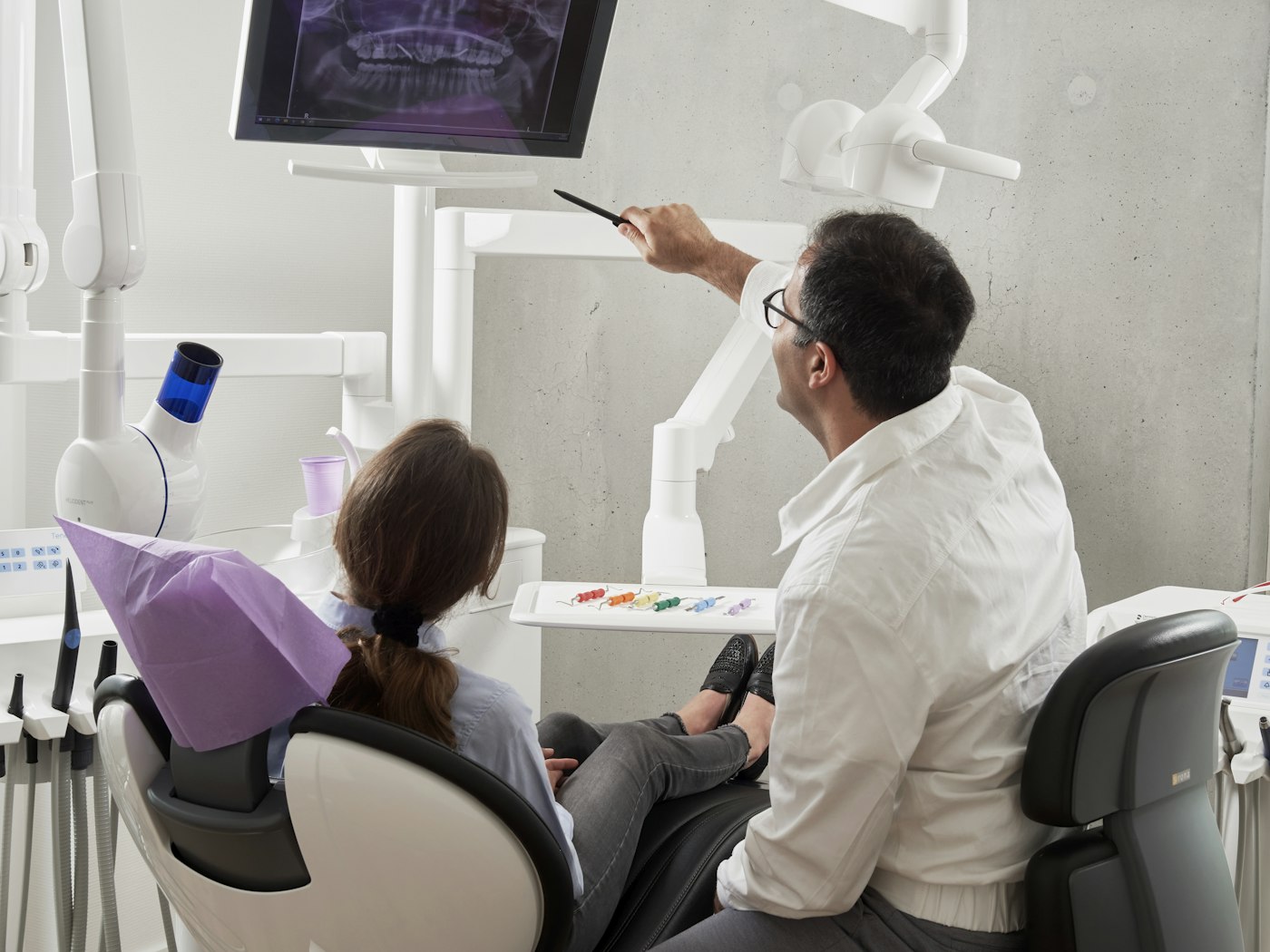 Cirurgião-dentista analisando radiografia com paciente em consultório moderno